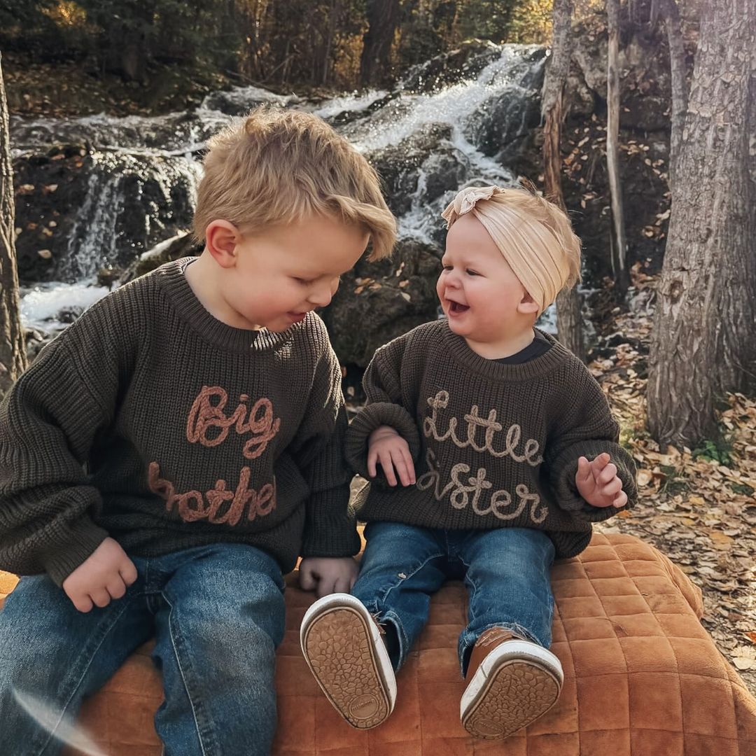 Siblings wearing matching Big Brother and Little Sister jumpers in dark green.