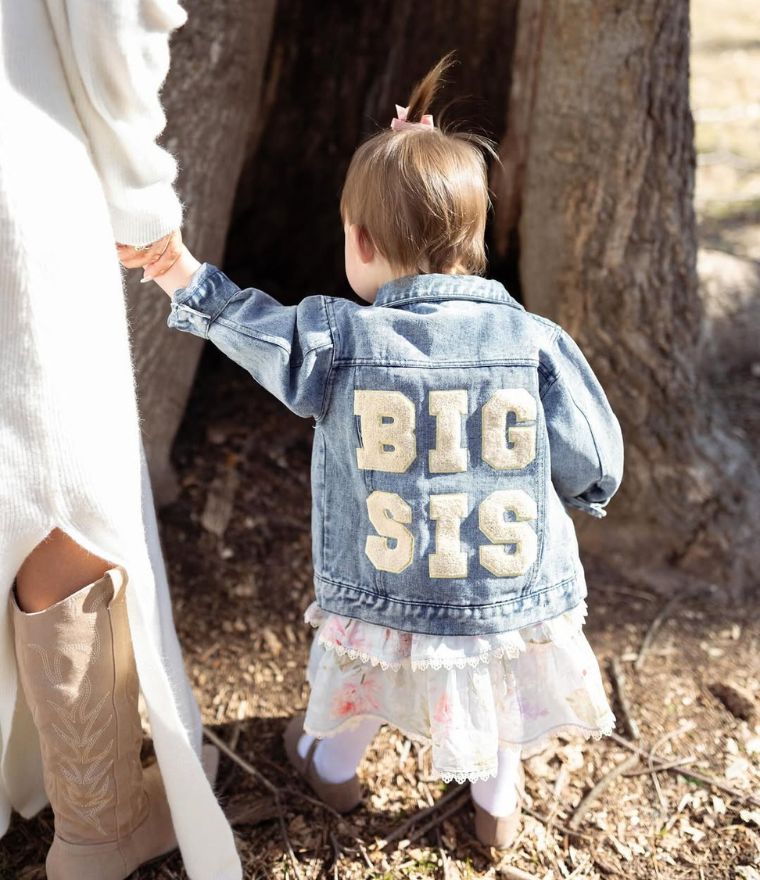 Toddler girl holding mum's hand, wearing Big Sis Denim Jacket