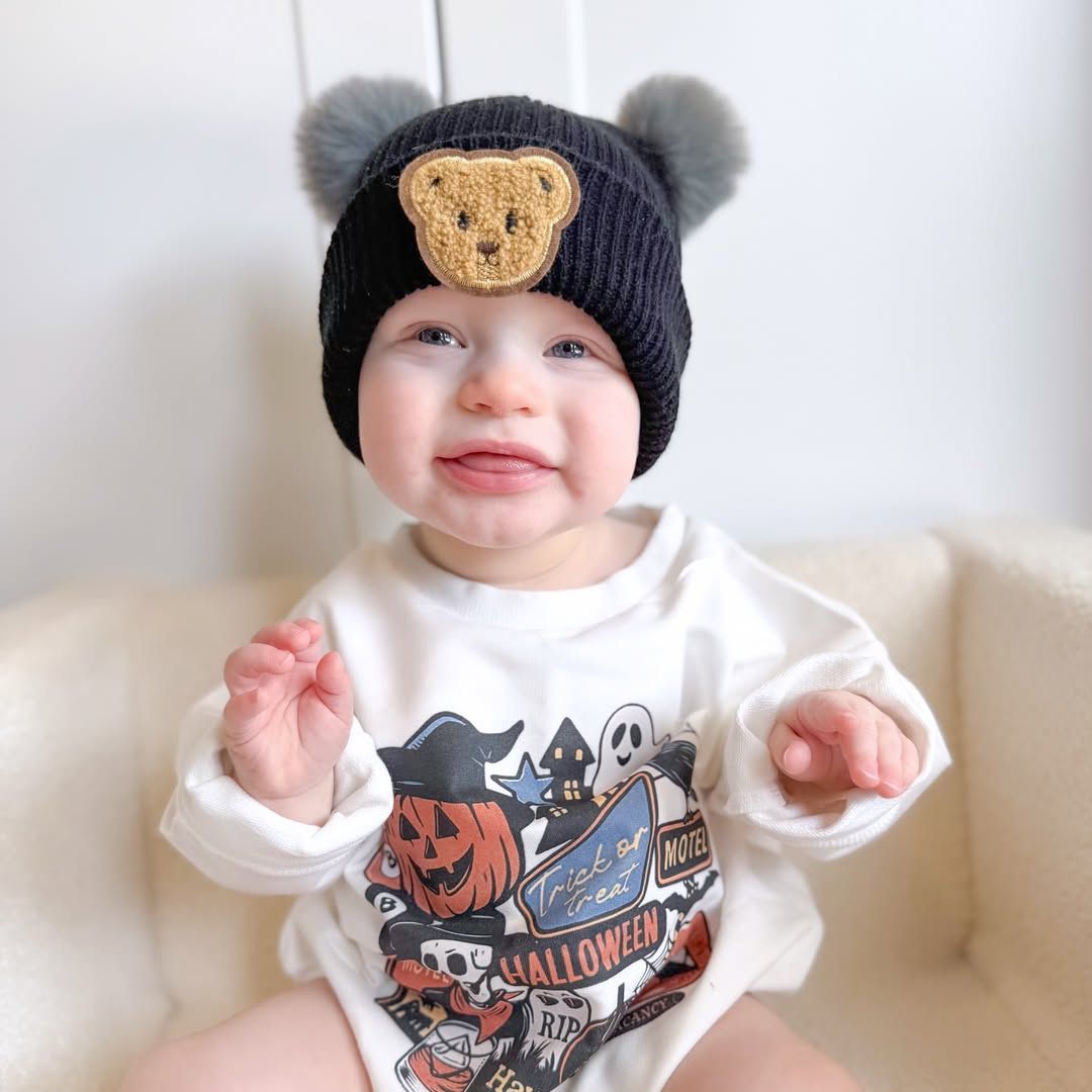 Baby boy wearing black ribbed beanie with pom poms and teddy bear motif