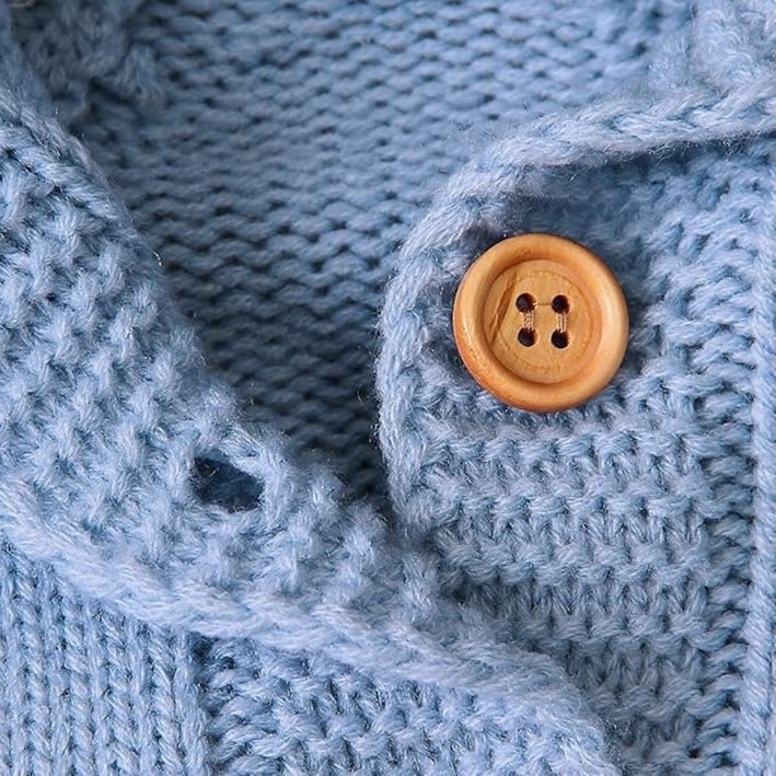 Detailed close-up of textured blue knit and wooden button on a baby bear romper