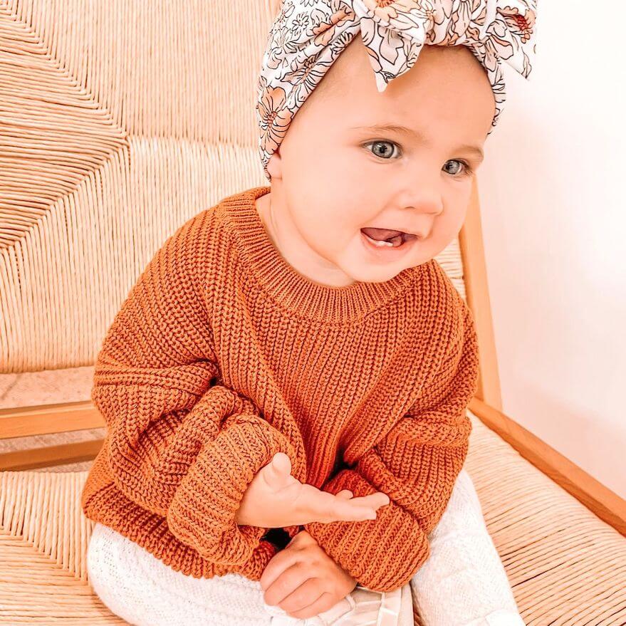 Baby girl wearing an oversized knitted jumper in a warm cinnamon colour