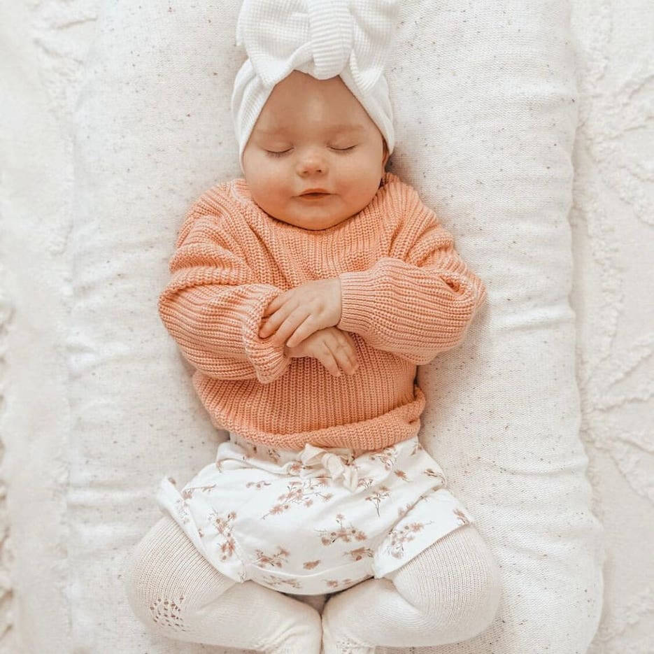 Baby girl asleep wearing our chunky knit jumper in baby pink
