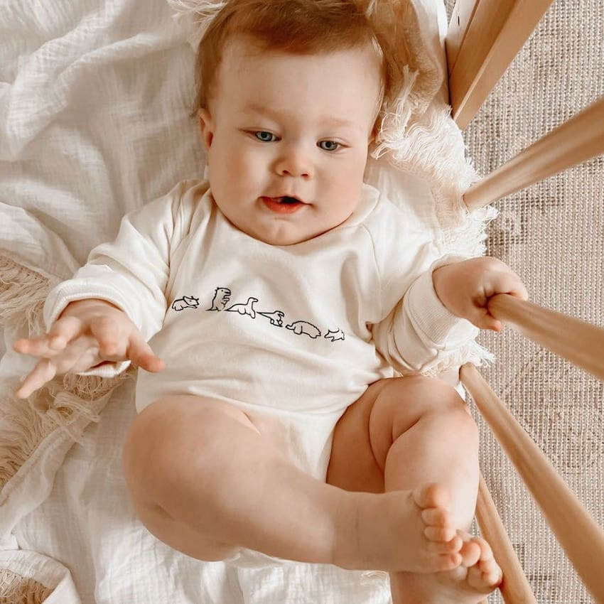 Baby boy wearing our Dino Long Sleeve Romper in creamy white