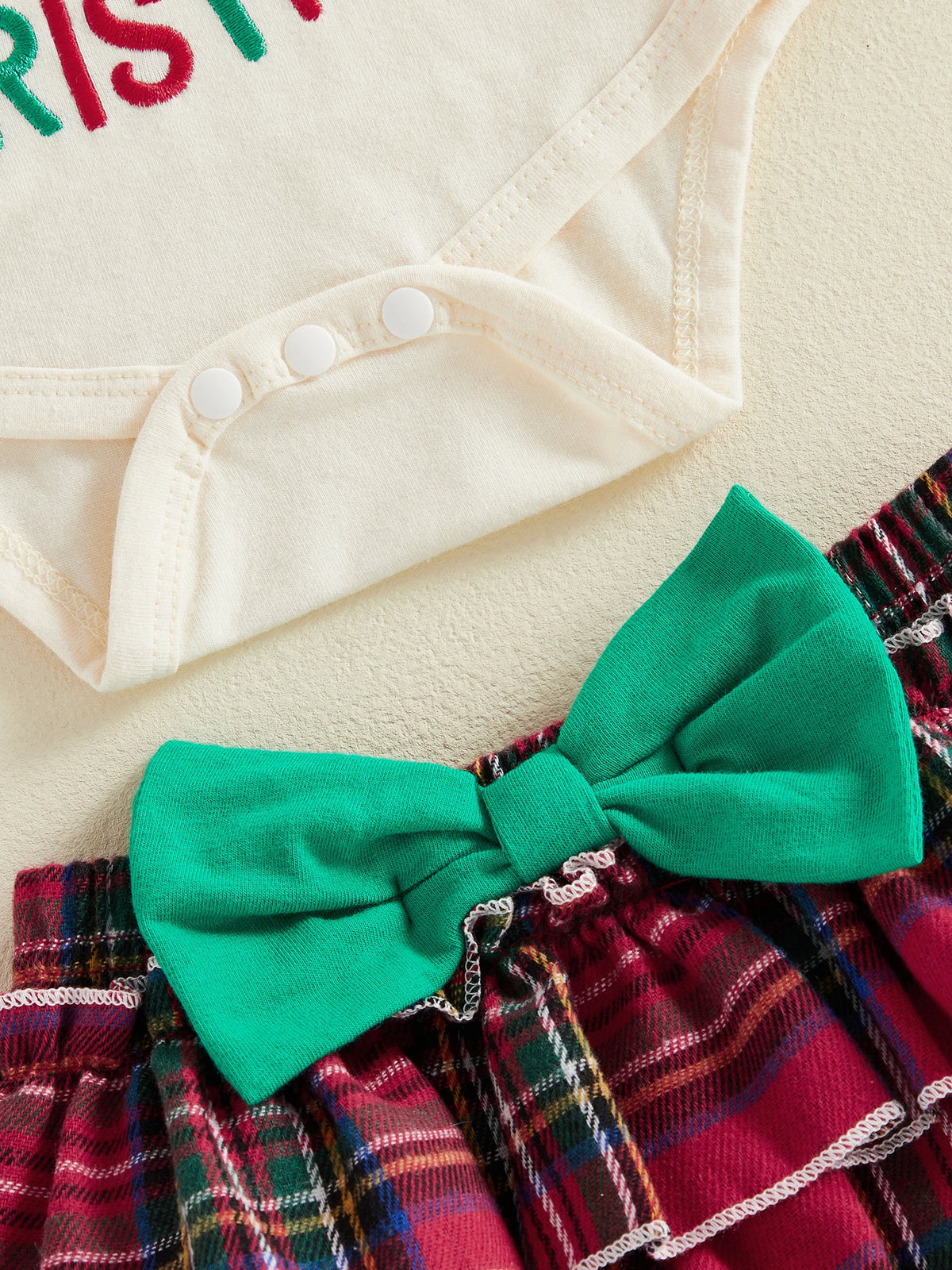 Close-up of baby girl outfit showing snap closures on the bodysuit and large green bow on tartan bloomer skirt