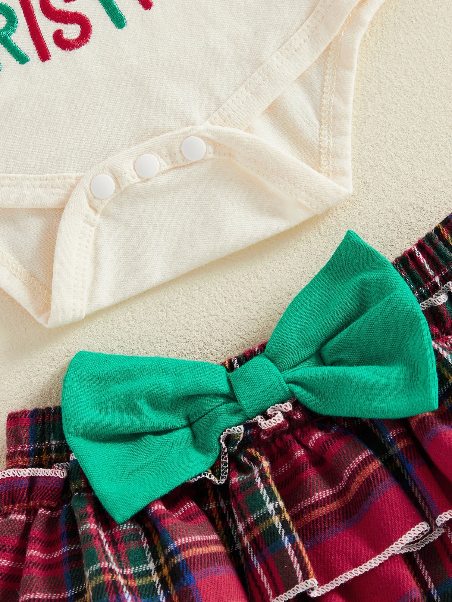 Close-up of baby girl outfit showing snap closures on the bodysuit and large green bow on tartan bloomer skirt