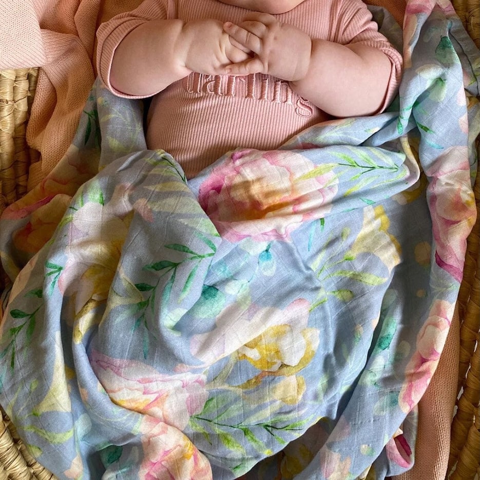 A baby wrapped in a Floral Muslin Wrap featuring soft, breathable fabric with a colorful floral design.