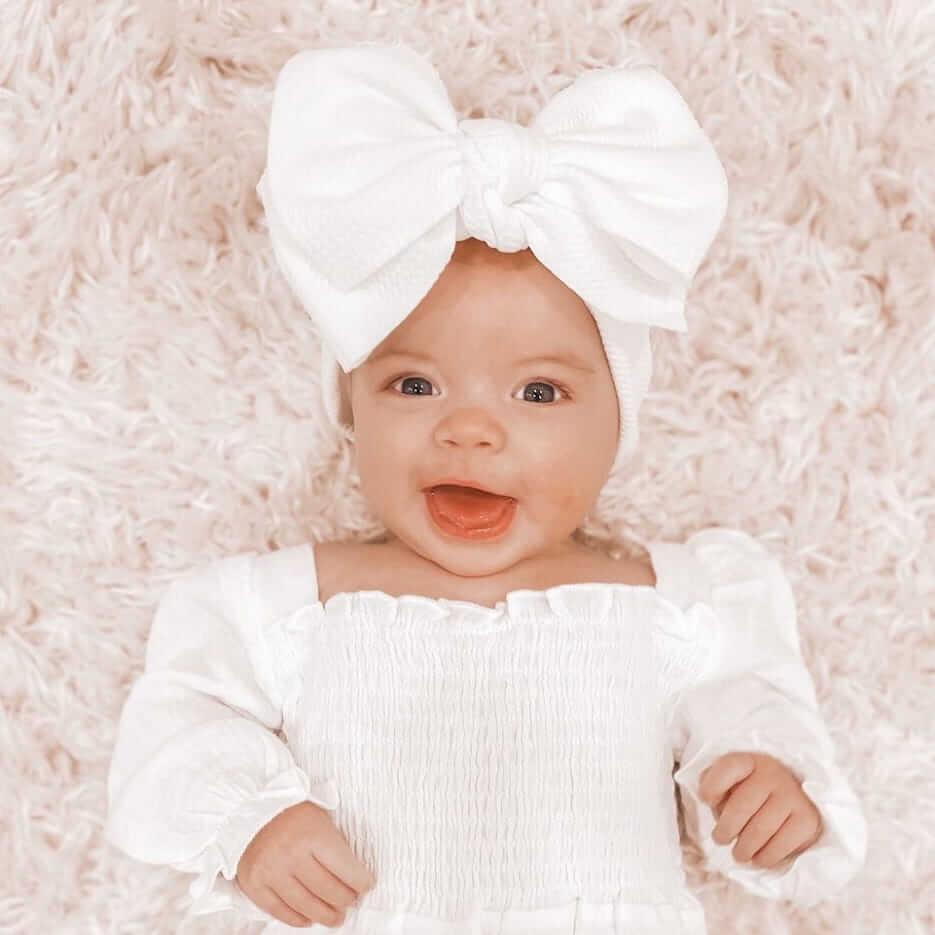 Baby girl wearing white bow headband from Lulu Babe