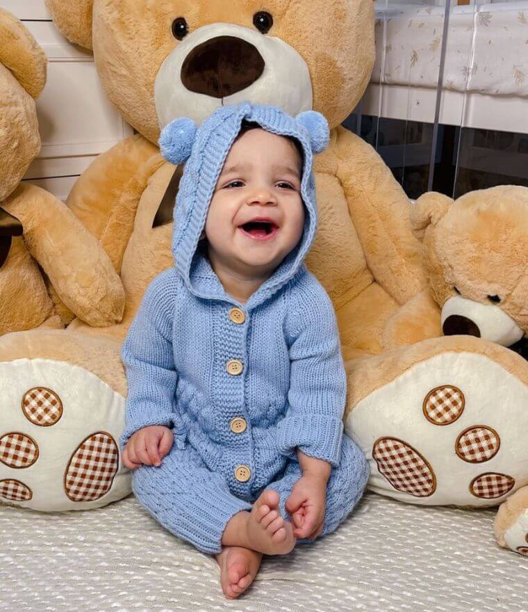 A happy baby boy wearing our blue Knit Baby Bear Onesie - sitting with large teddy bears.