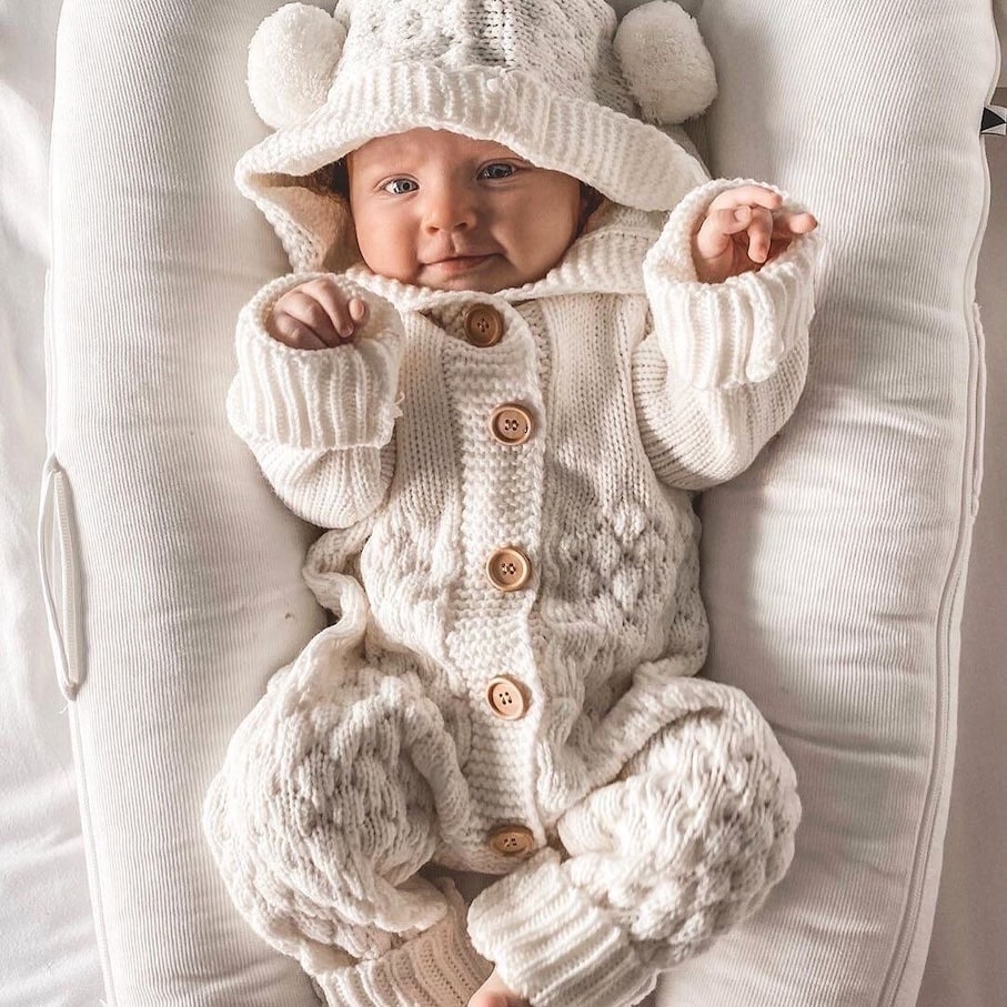 Baby boy wearing a cosy white knit bear onesie with hood and pom-pom ears. Adorable and warm baby outfit.