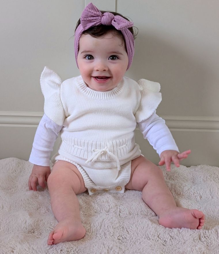 Cute baby girl wearing knit ruffle romper in white from Lulu Babe