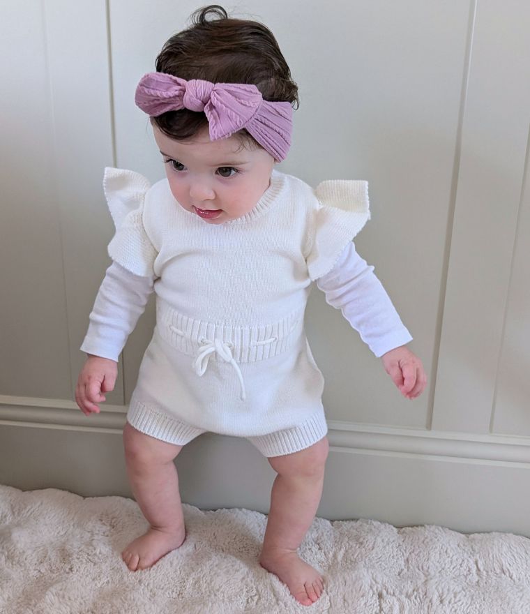 Baby girl wearing knit ruffle romper in white from Lulu Babe
