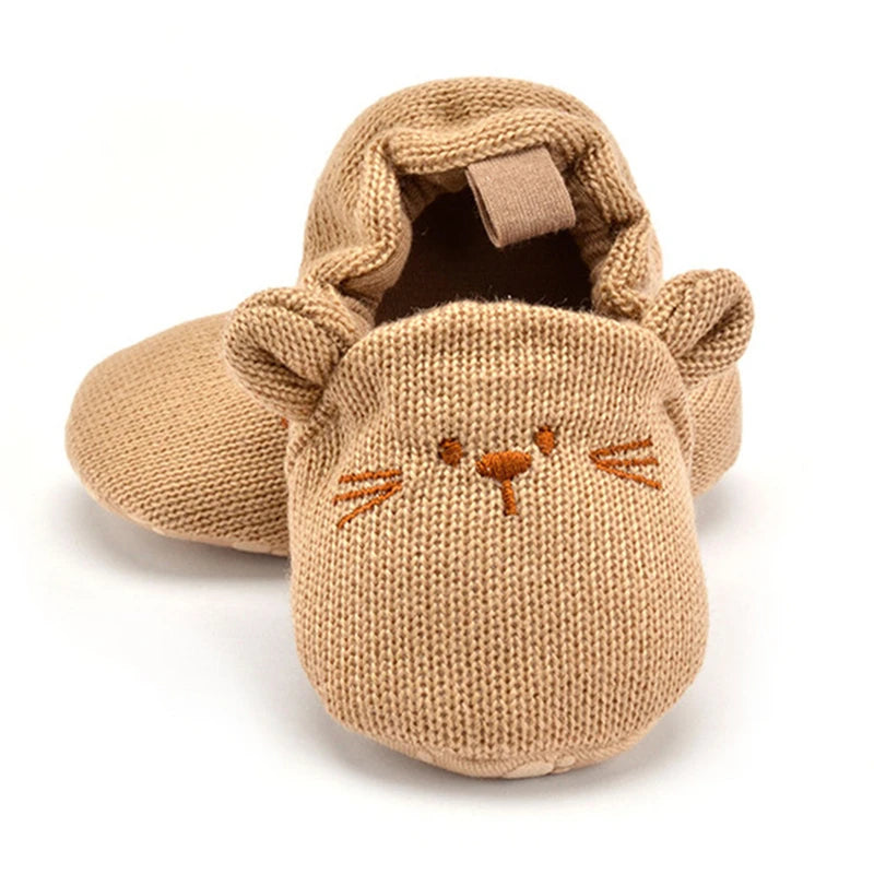 Adorable tan knitted cat baby booties with 3D ears, whiskers, and a secure slip-on design for cosy little toes.