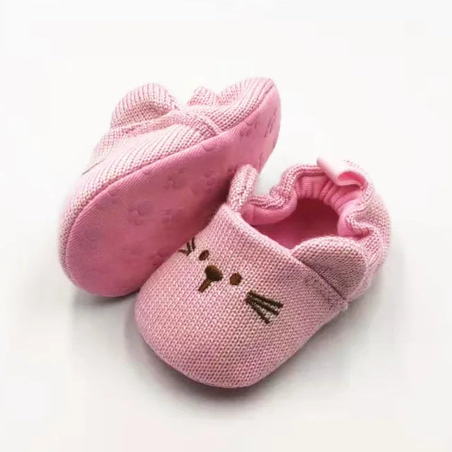 Adorable pink knitted cat baby booties with 3D ears, whiskers, and a secure slip-on fit for cozy little toes.