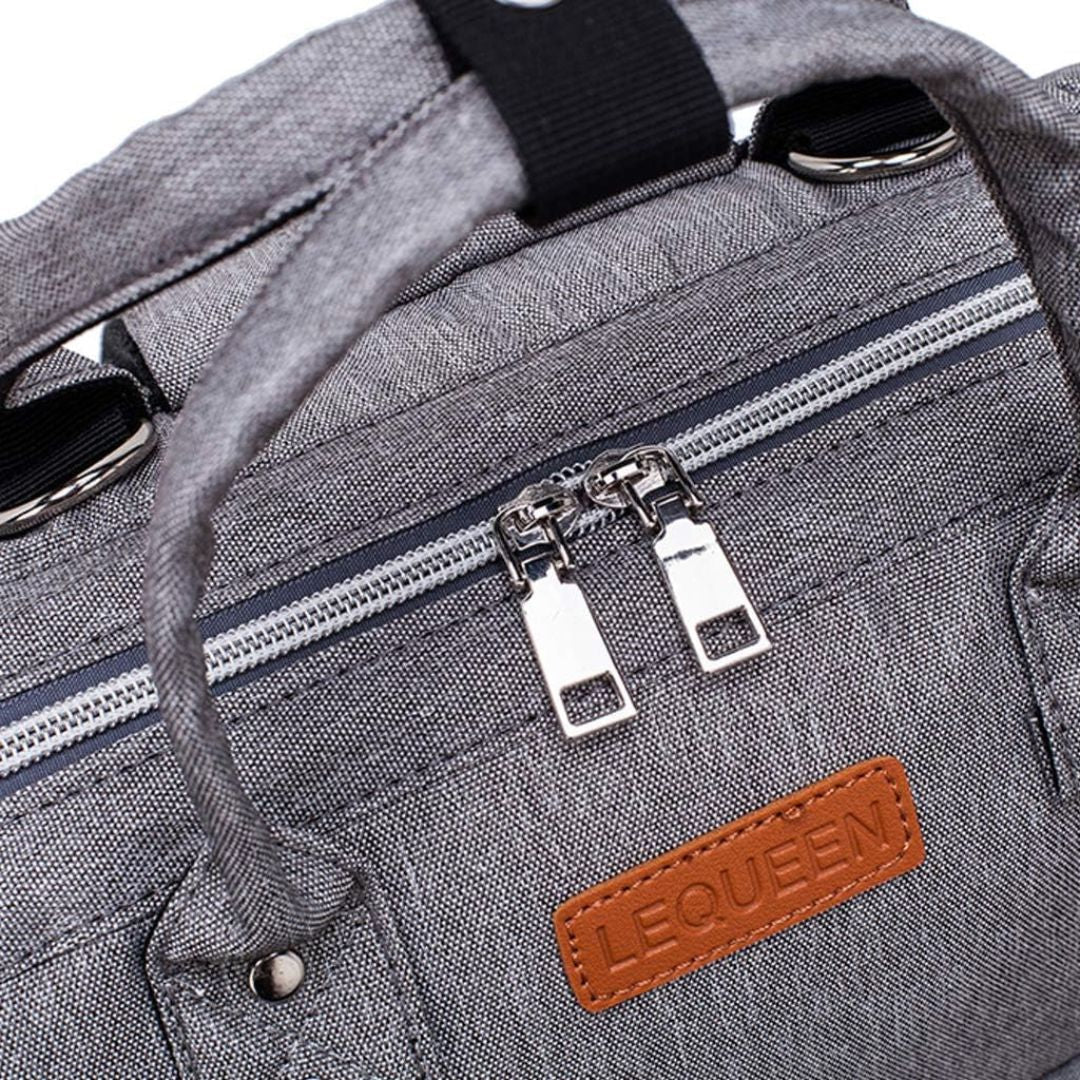 Close-up of LeQueen Quilted Nappy Backpack zipper and logo, showcasing stylish grey fabric design.