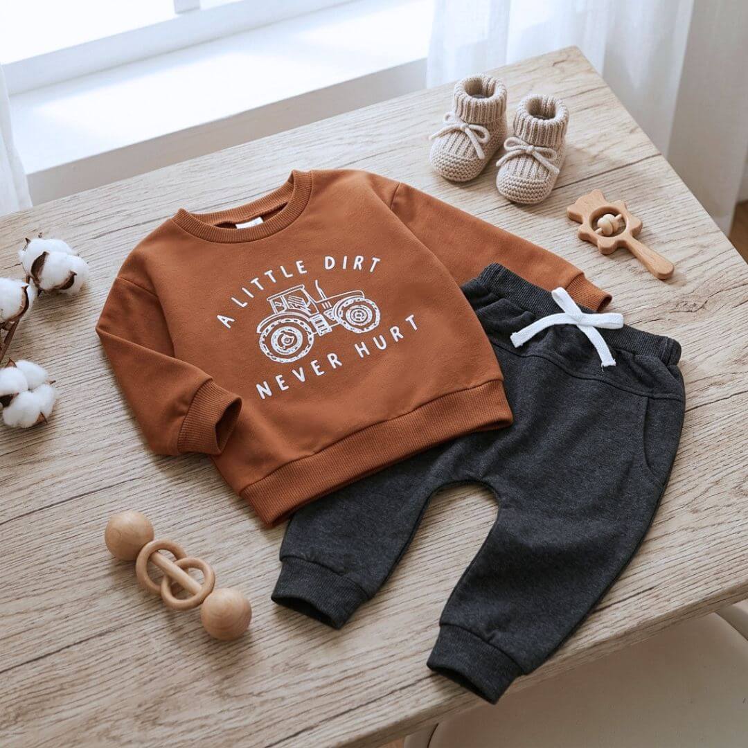 Baby clothing set laid flat, featuring a rust sweatshirt with a white tractor graphic paired with dark charcoal grey pants