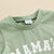 Green baby boy outfit - Mama's Boy top and check shorts - closeup