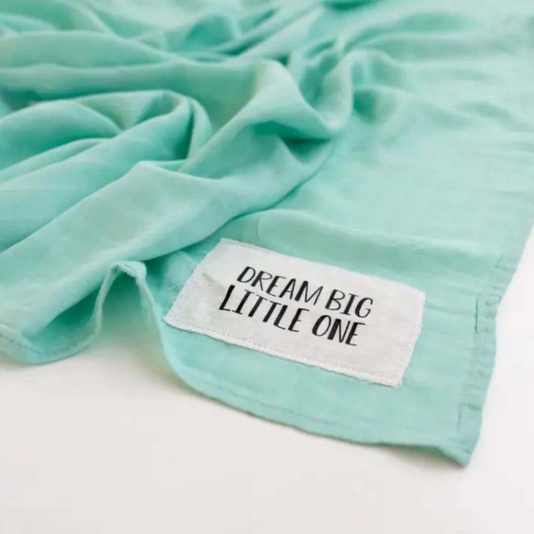 Dream Big mint muslin swaddle blanket for baby, featuring a cute patch that says 'Dream Big Little One'.