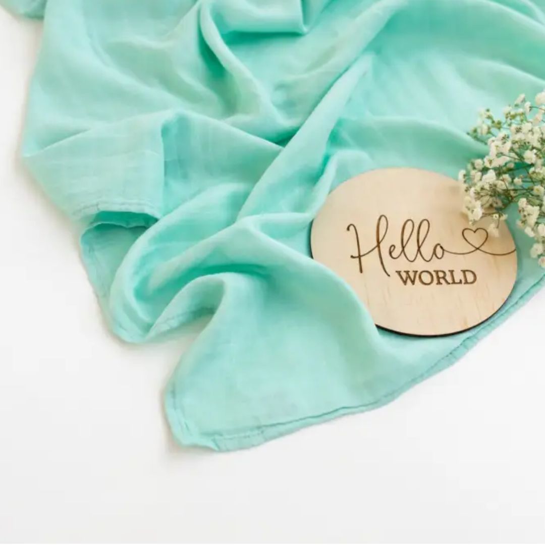 Mint muslin baby swaddle with 'Hello World' patch, perfect for newborn photos
