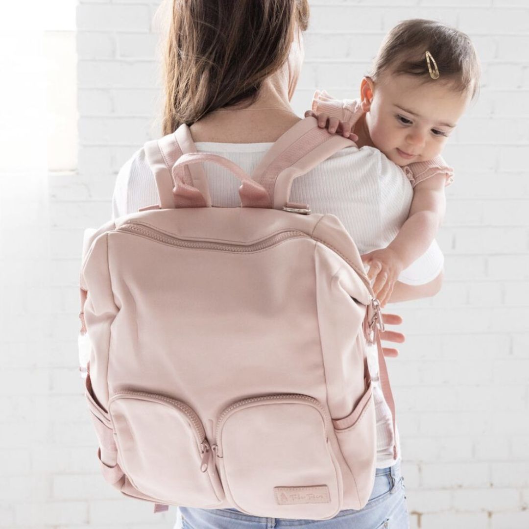 A mum wearing her blush pink neoprene nappy backpack, holding a baby