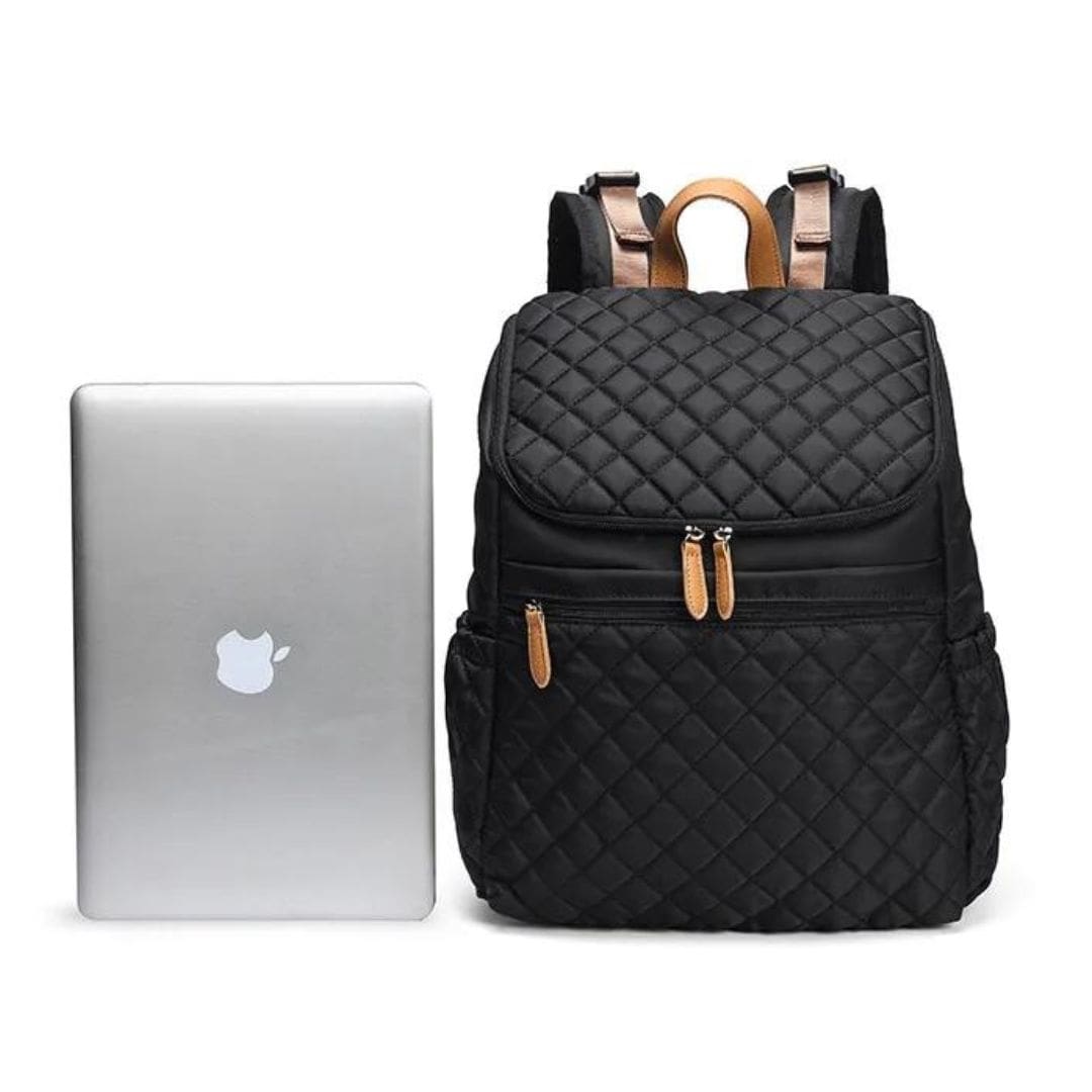 Stylish black quilted nappy backpack beside a laptop, perfect for modern parents on the go.