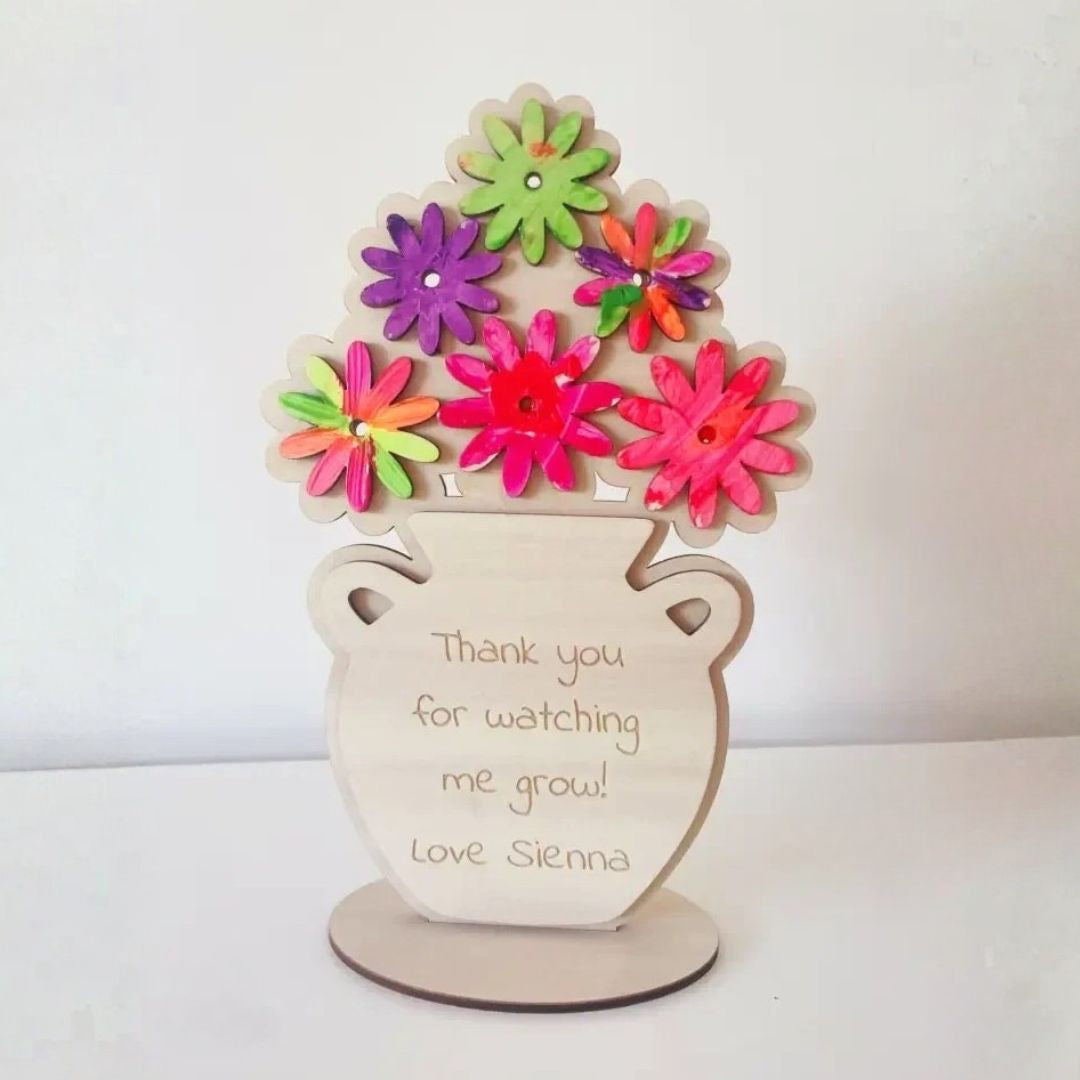 Completed personalised wooden flower vase with painted fluorescent daisy flowers and engraved message reading "Thank you for watching me grow"