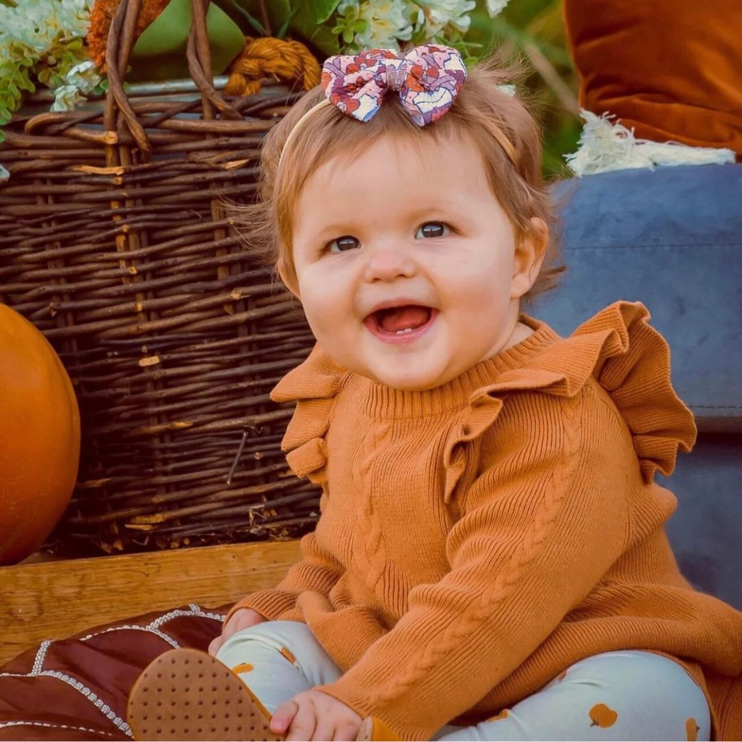 Smiling baby girl wearing Poppy winter baby dress in cinnamon from Lulu Babe