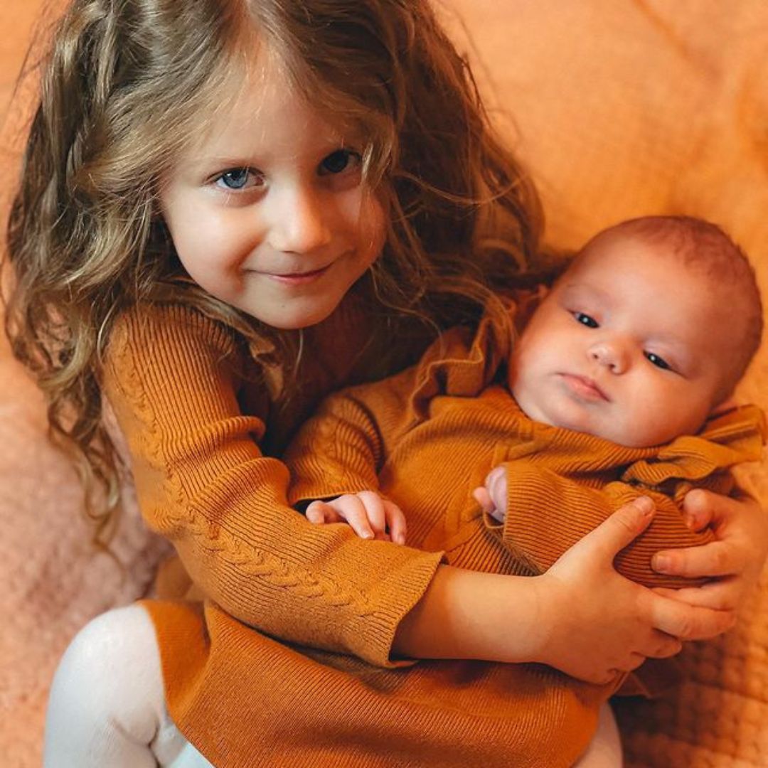 Sisters wearing matching winter baby dresses in cinnamon from Lulu Babe