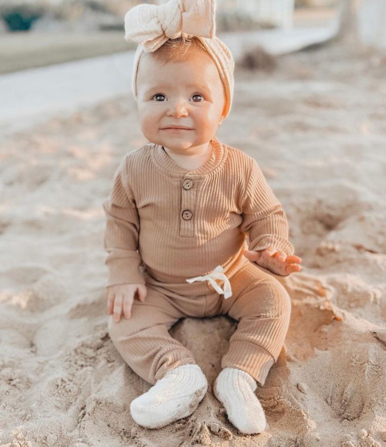 Baby girl sitting on sandy beach wearing ribbed long sleeve bodysuit and pants outfit in latte - Lulu Babe