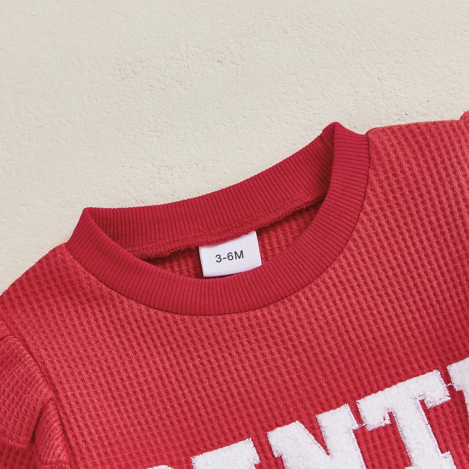 Close-up of the Santa Baby Ruffle Romper neckline, showcasing its soft red waffle knit fabric and ruffle details for baby girl Christmas outfit.
