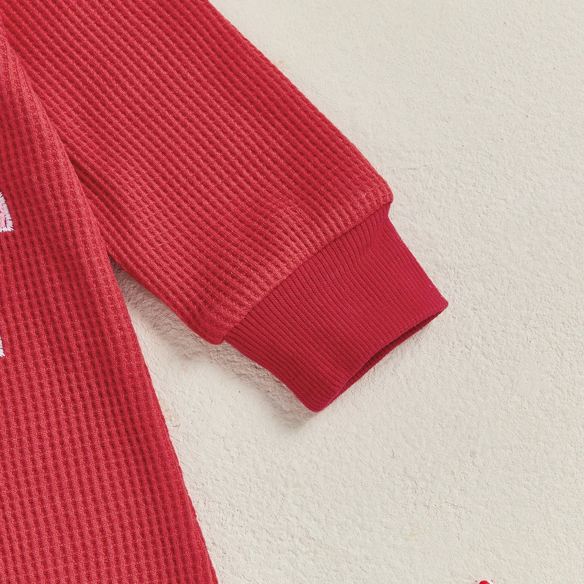 Close-up of the ruffled sleeve of a red long sleeve romper for baby girls, perfect festive Christmas outfit.