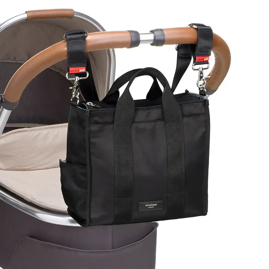 Stylish black Storksak nappy bag attached to stroller handle, designed for convenient baby essentials storage.