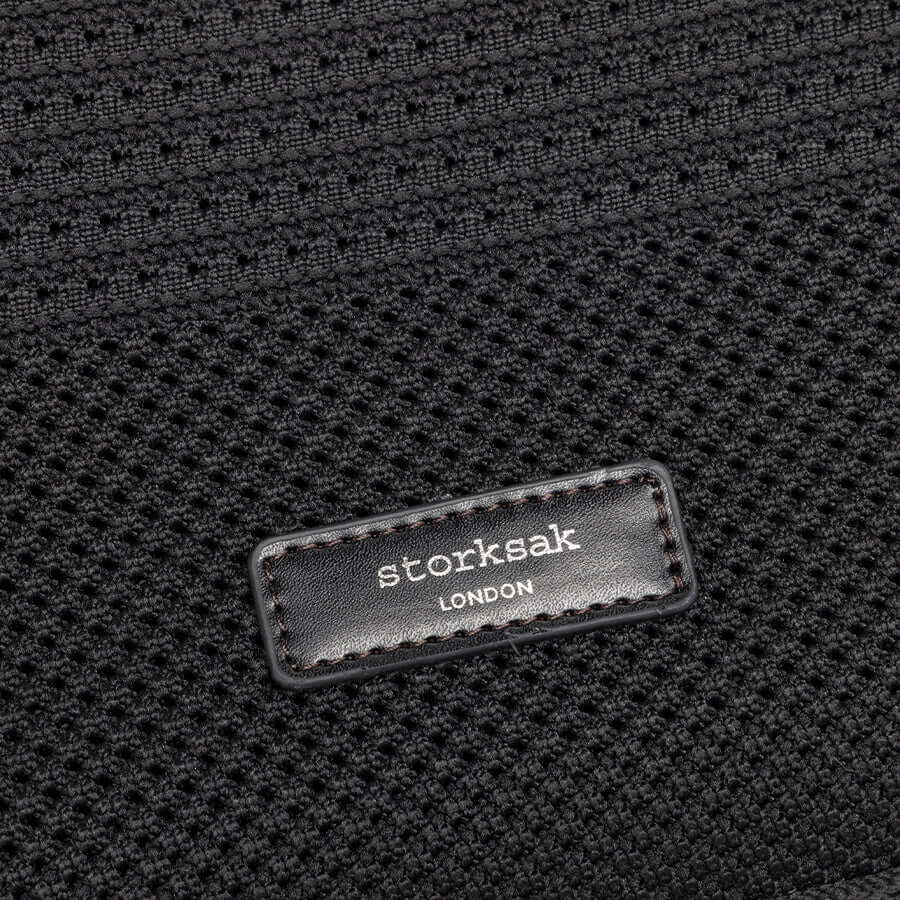 Close-up of Storksak London logo on woven black fabric, showcasing premium design of Thea Tote bag.