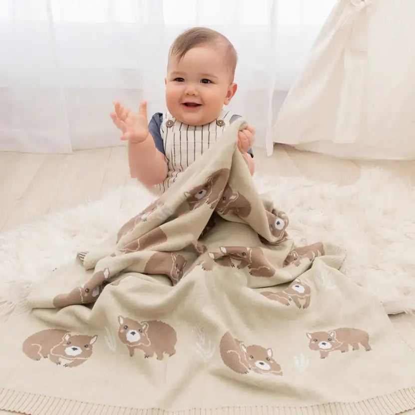 Happy baby playing with a soft cotton wombat baby blanket, perfect for prams and newborn snuggles.