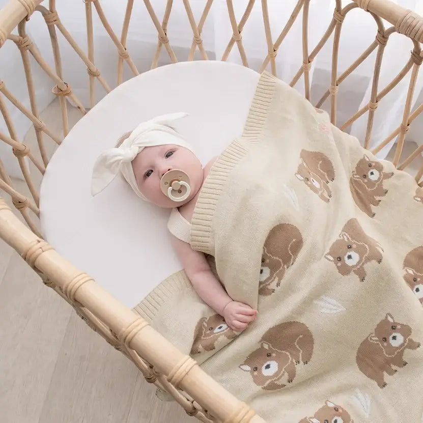 A cozy baby wrapped in a soft cotton wombat blanket in a bassinet, perfect for newborns and prams.