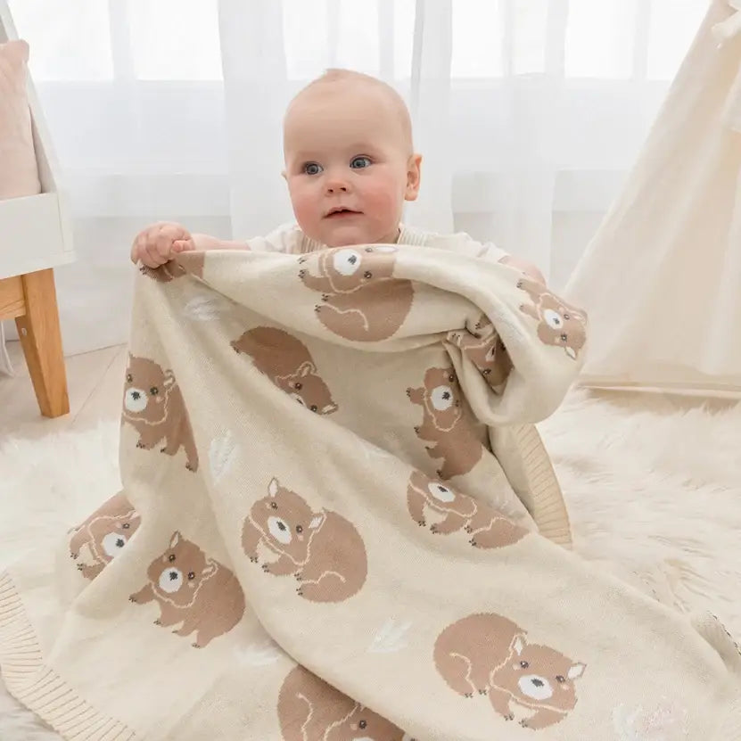 Sweet baby engaging with a cosy wombat baby blanket, perfect for prams and newborn comfort.