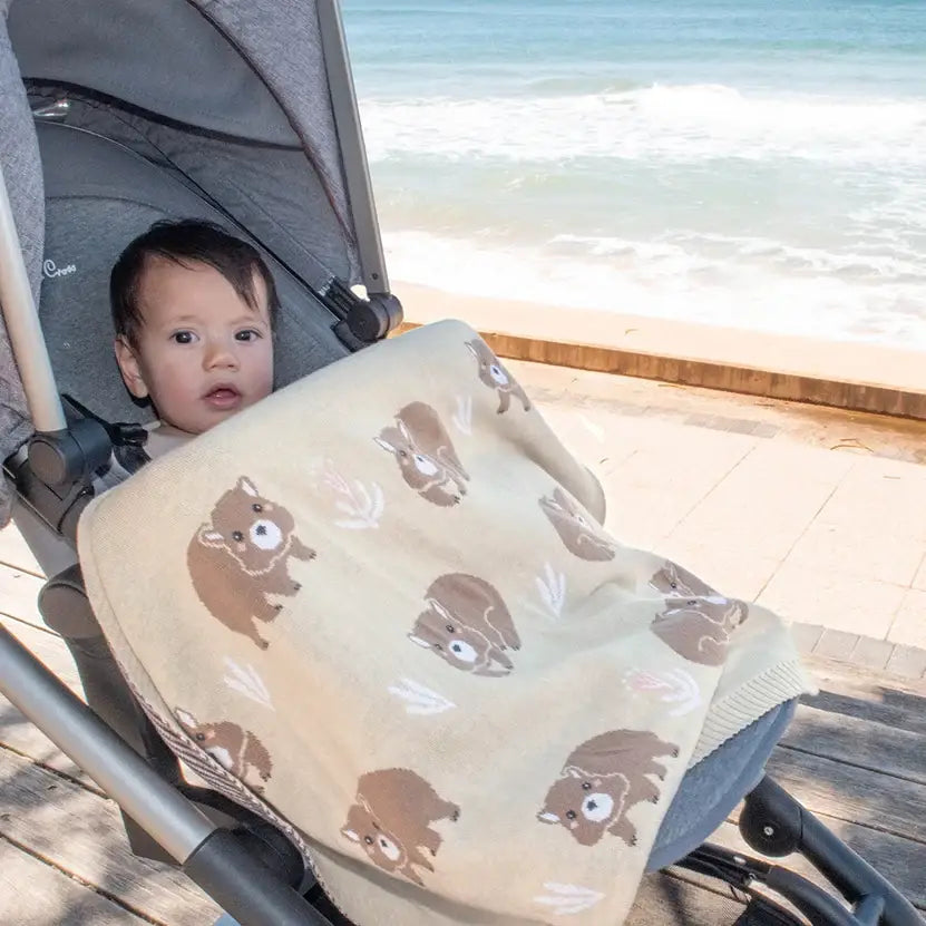 Cute baby covered with a cosy wombat blanket in a pram by the beach, perfect for warm and lightweight comfort.