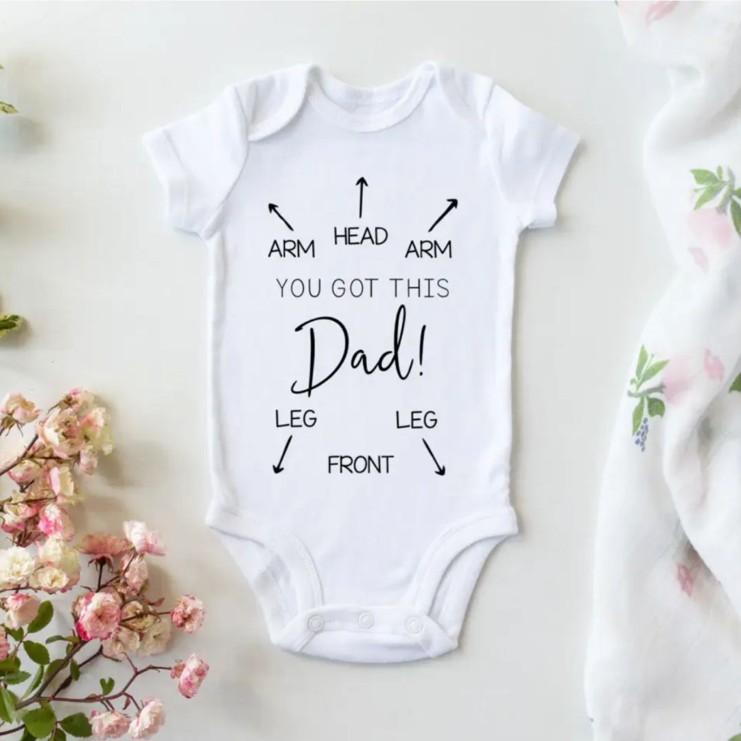 White baby bodysuit with "You Got This Dad" print and directional arrows pointing to body parts
