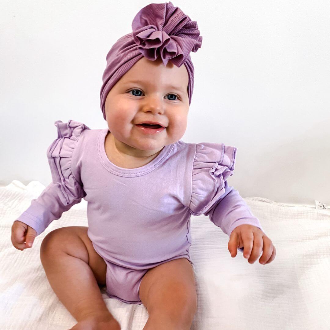 Baby girl wearing lavender long sleeve flutter bodysuit and flower turban