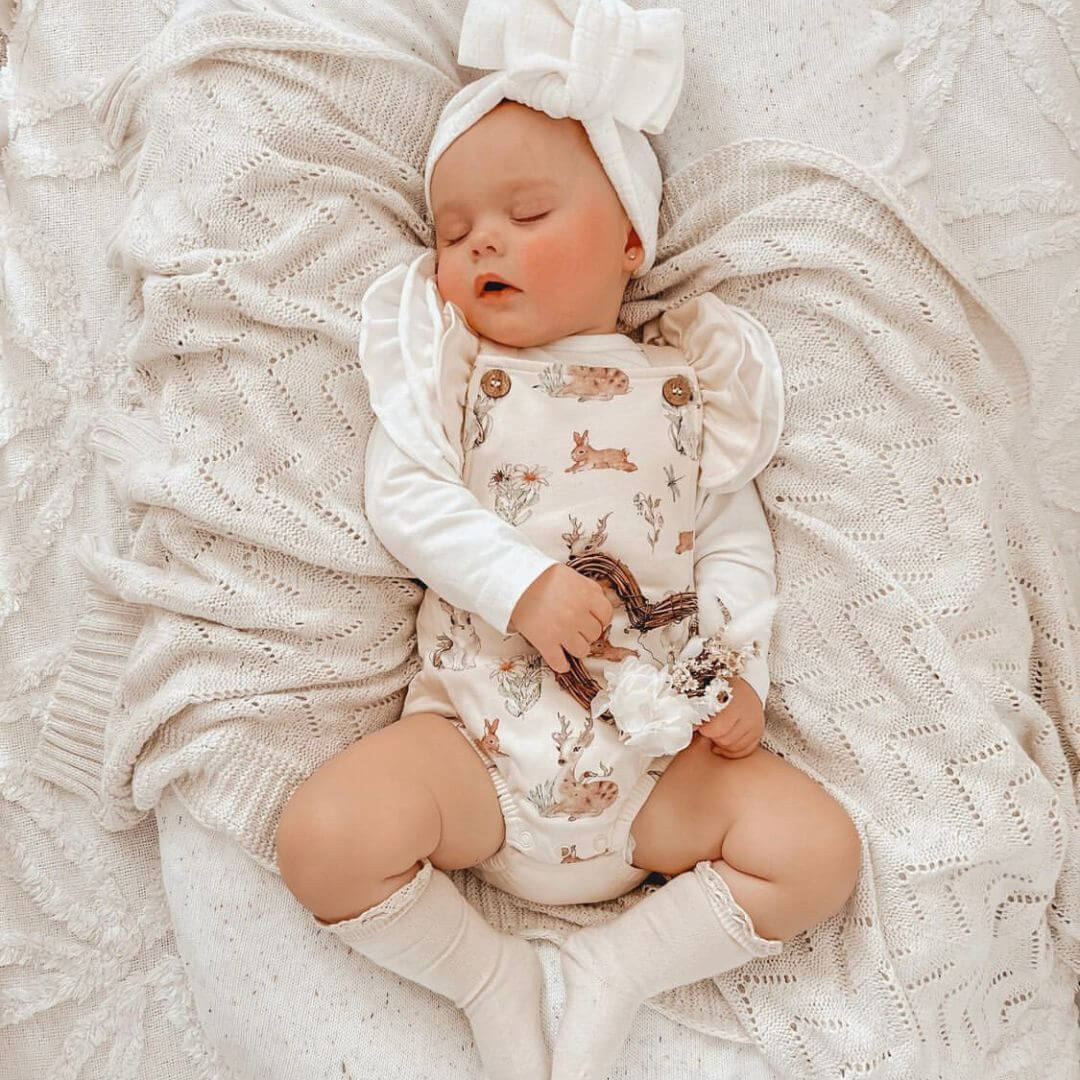 Sleeping baby girl wearing white long sleeve flutter bodysuit layered under romper