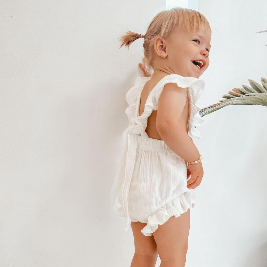 Toddler girl wearing white ruffle baby romper, smiling