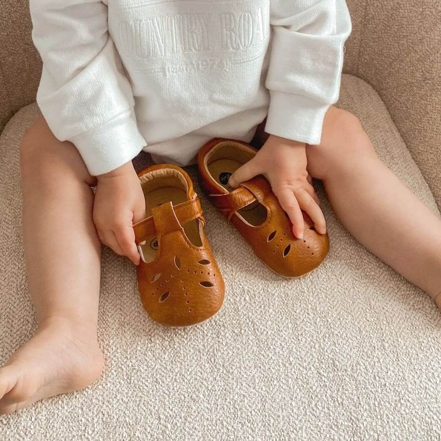 Baby holding Cutout T-Bar Baby Shoes in tan vegan leather