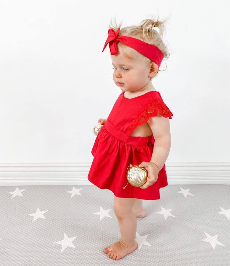Baby girl wearing red lace romper dress from Lulu Babe, holding Christmas decorations