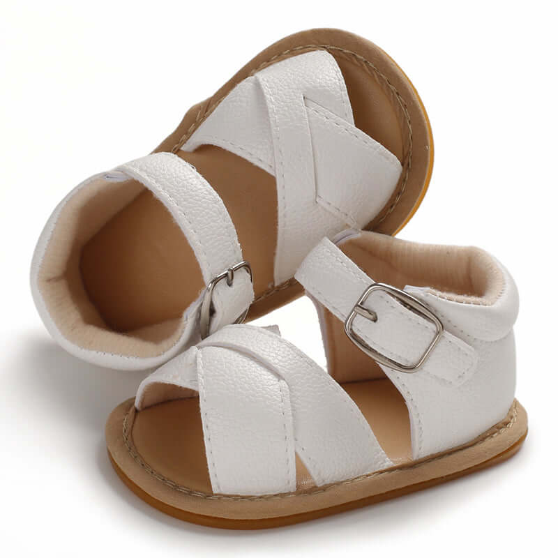 White baby sandals with crossover front strap, enclosed heel, adjustable velcro ankle strap and faux buckle detail